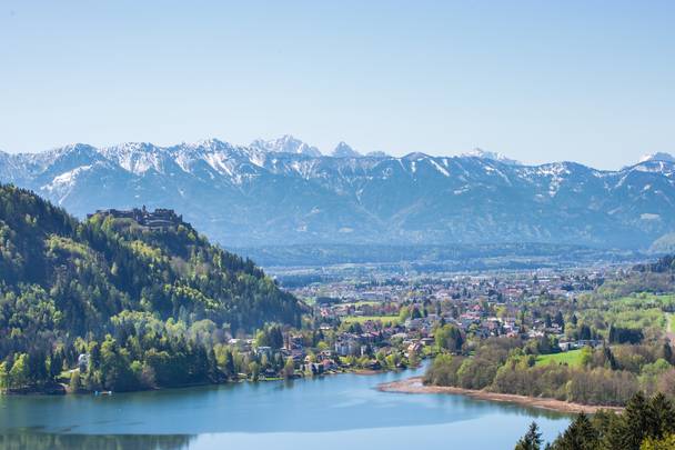 <p>Blick über den sonnigen und frühlingshaften Ossiacher See in Richtung der Draustadt Villach mit der Burg Landskron auf der linken Seite und den Karawanken im Hintergrund. Im hellblauen Himmel leuchten die schneebedeckten Bergspitzten der südlichen Karawanken. Das Wasser des Ossiacher Sees, dem drittgrößen See Kärntens, schimmert blau und die Landschaft von hellgrün bis dunkelgrün. Die Burg Landskron beheimatet auch eine Adlerarena mit einem in Europa einzigartigem Greifvogelpark.</p>