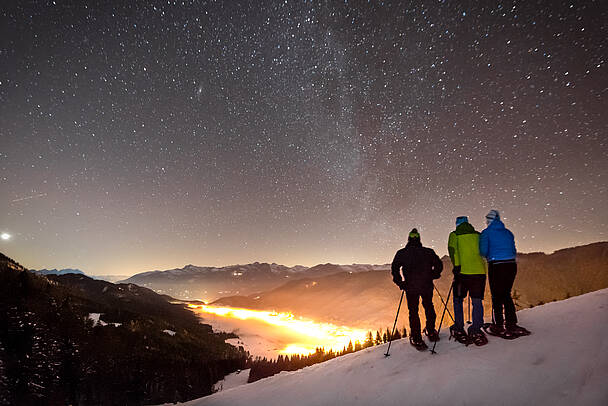 Winterwanderer genießen den Sternenhimmel über dem Weissensee in verschneiter Wintelandschaft.