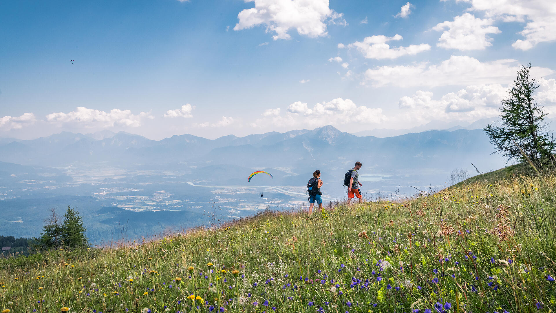Pärchen beim Wandern auf der Gerlitzen Alpe mit Paragleiter im Hintergrund